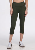 A person wears Woolx Merino Flex® McKenna Capris in Everleaf, featuring a high-waisted, comfortable, moisture-wicking merino wool blend—ideal for all-day wear—paired with white sneakers with black stripes against a white background. | Jessica is 5’10”, wearing a size S