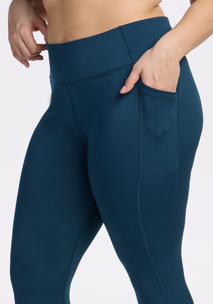 A person models Woolx Merino Flex® McKenna Capris in Majolica Blue, showing the mid-torso to mid-thigh area, with one hand in the side pocket against a plain background.