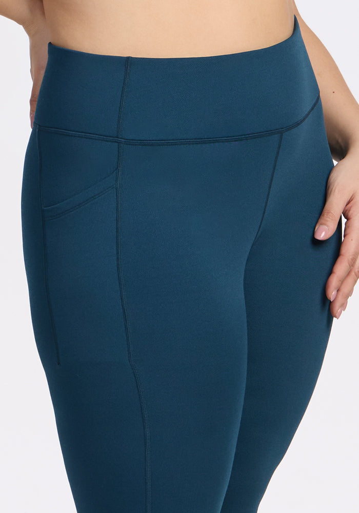 A close-up of a person wearing Woolx Merino Flex® McKenna Capris in Majolica Blue, featuring high-waisted, moisture-wicking fabric and a side pocket, shown from lower torso to upper legs against a plain white background.