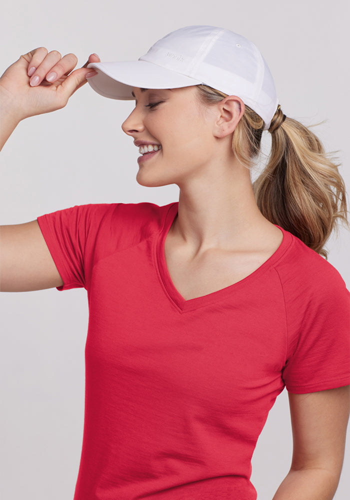 Woman in Woolx Mia V Neck - Berry Ice Pop and white cap, facing sideways, holding the brim with one hand.