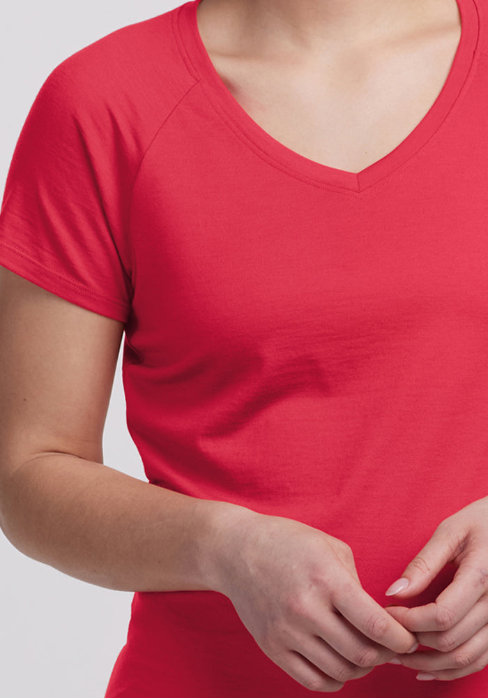 A person in a red Woolx Mia V Neck - Berry Ice Pop merino tee stands with hands loosely clasped.