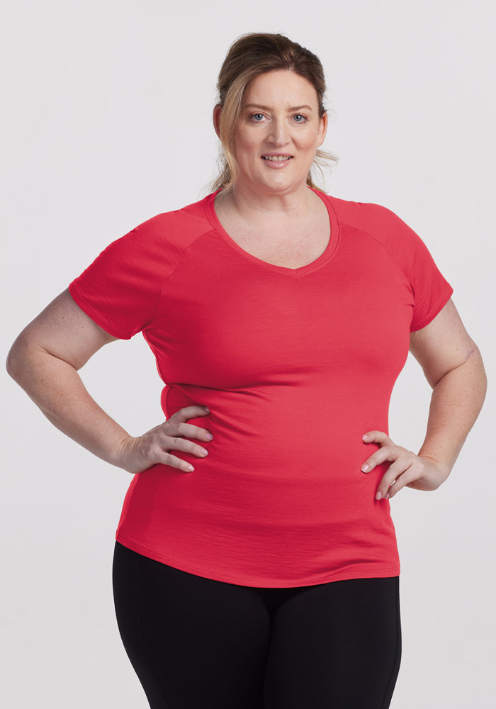 Woman with light brown hair in a ponytail wears Woolx Mia V Neck - Berry Ice Pop, black pants, stands smiling. | Cambre is 5’11”, wearing a size XL
