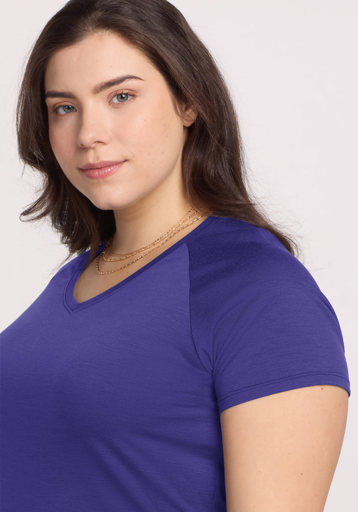 Woman with long brown hair wears the Woolx Mia V Neck in Berry Indigo and gold necklaces, smiling softly at the camera.