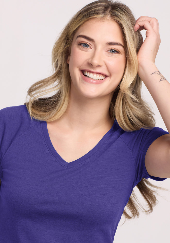 Smiling woman in Woolx Mia V Neck tee in Berry Indigo, touching her long blonde hair.