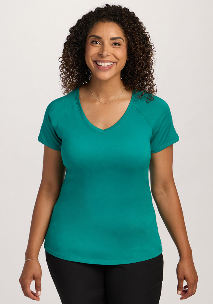 Smiling woman with curly hair wears Woolx Mia V Neck - Cabana Crush, standing against a plain light background. | Kisha is 5’8”, wearing a size M