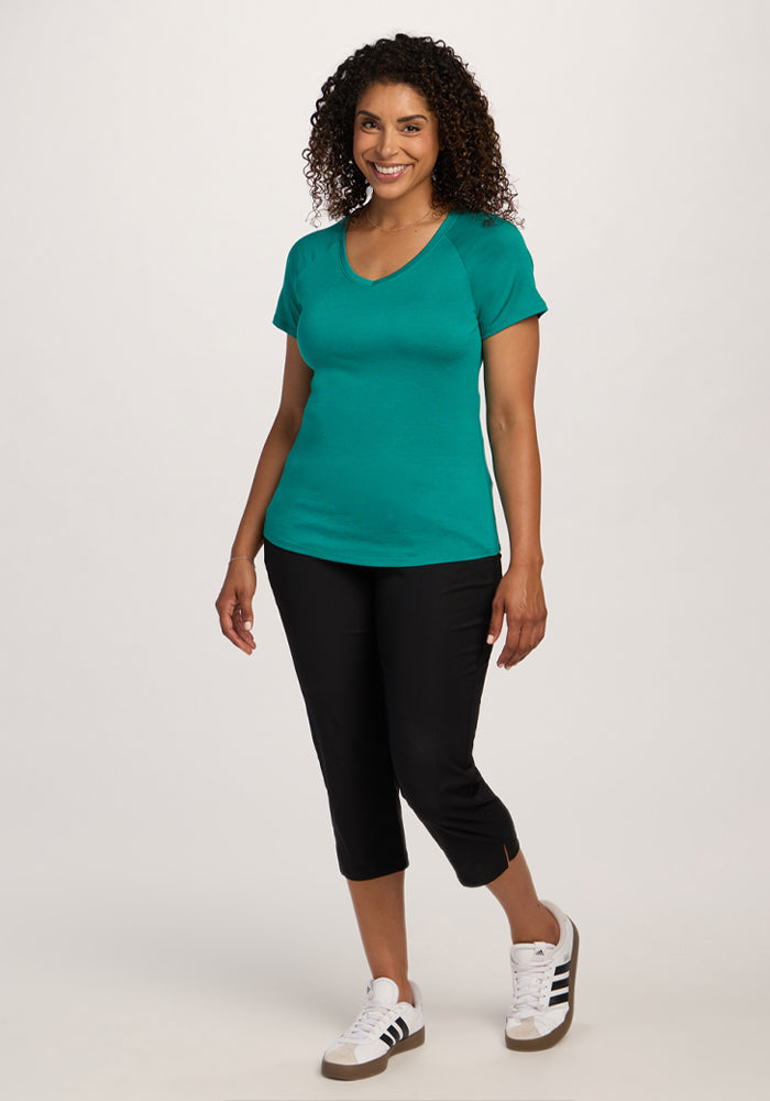 Woman smiling in a Woolx Mia V Neck - Cabana Crush tee and black capris, perfect travel wear, against a white backdrop.