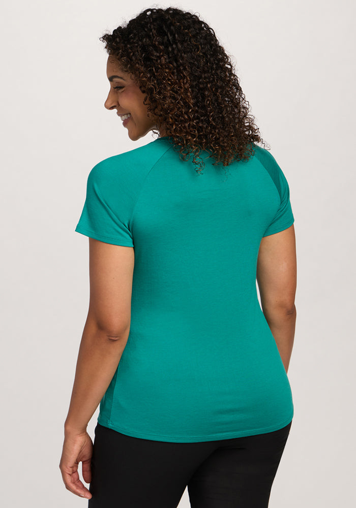 Smiling woman with curly hair in Woolx Mia V Neck - Cabana Crush, black pants, facing away from the camera.