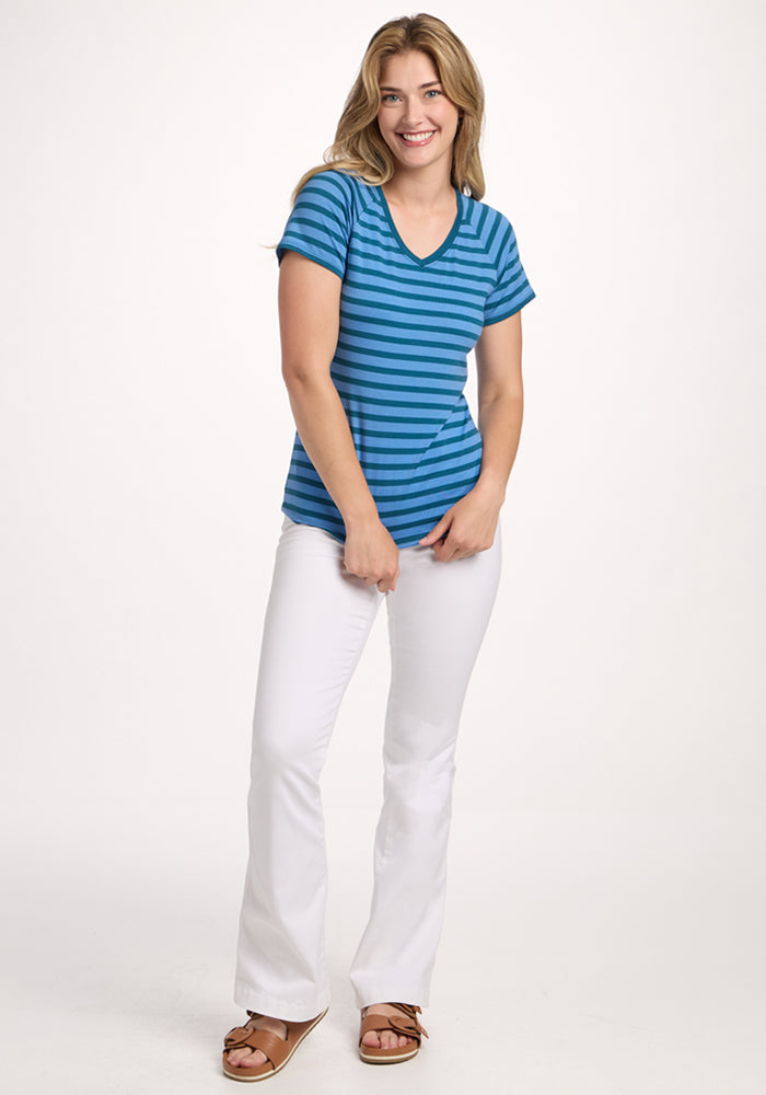 A woman wearing the Woolx Mia V Neck - Coastal Stripe women’s Merino wool tee, white pants, and brown sandals stands smiling against a plain white background.