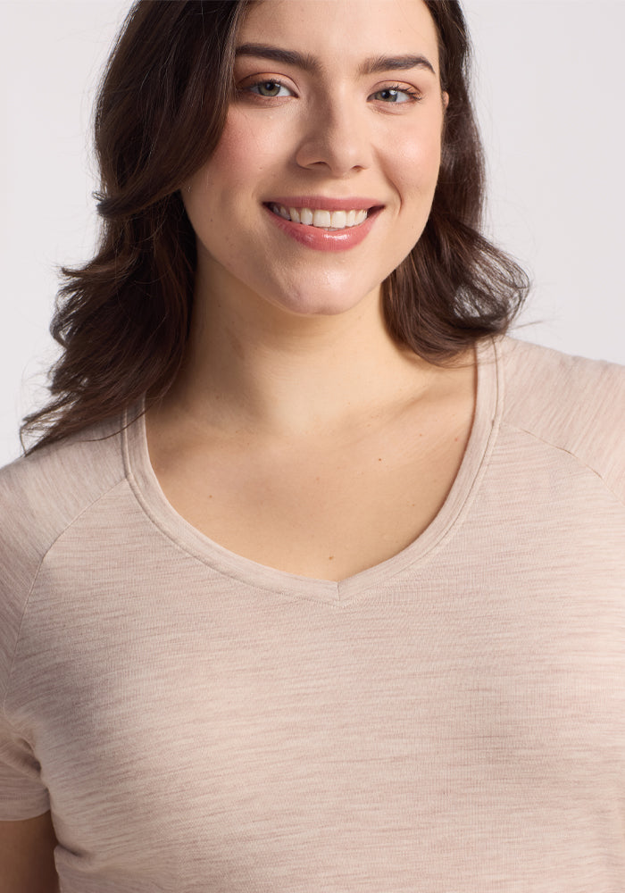 A person with long brown hair smiles, wearing the Woolx Mia V Neck in Cream Heather against a plain white background.