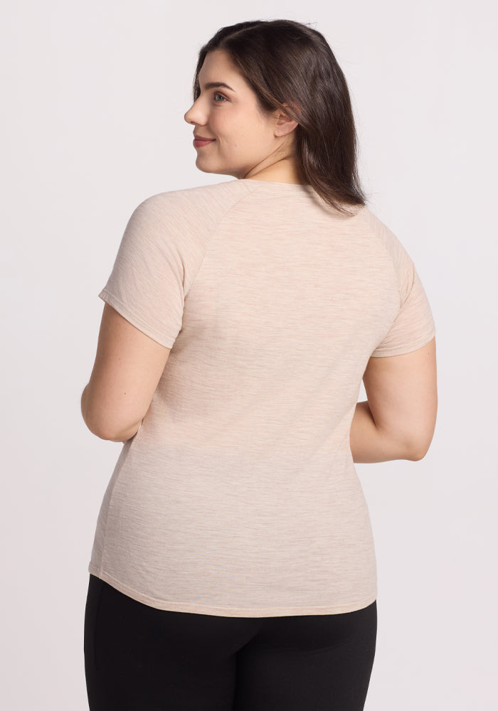 A person with long dark hair and a warm smile stands in Woolx's Cream Heather Mia V Neck and black pants, turning slightly to the side against a plain white background.