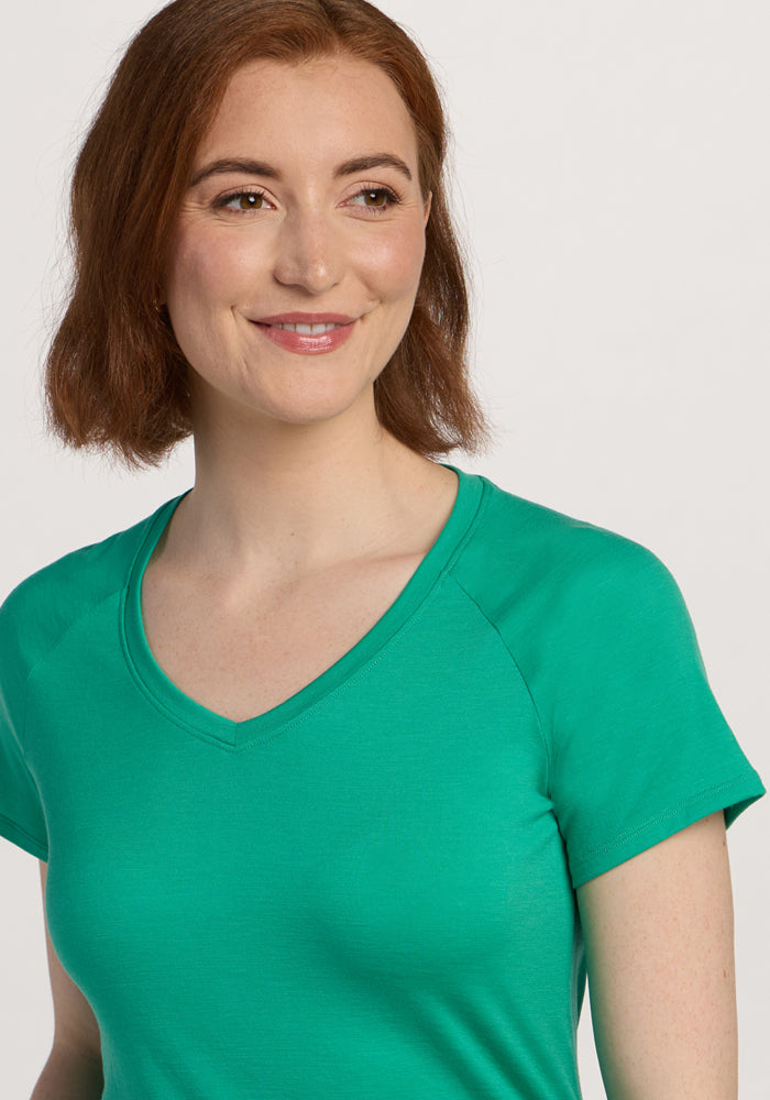 Woman with short brown hair smiles, wearing the Woolx Mia V Neck - Jungle and looking slightly to the side.