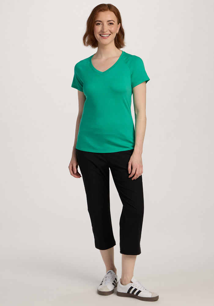 Smiling woman wearing the Woolx Mia V Neck - Jungle with black capri pants and sneakers against a plain background.