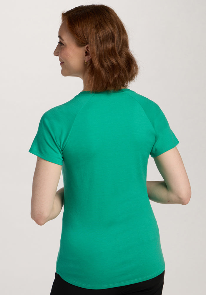Woman with wavy brown hair wears the Woolx Mia V Neck - Jungle, seen from the back, smiling and looking left.