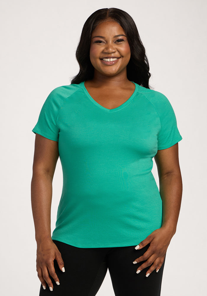 Smiling woman wears the Woolx Mia V Neck - Jungle with black pants, standing against a plain light background. | Sapphire is 5’8”, wearing a size XL