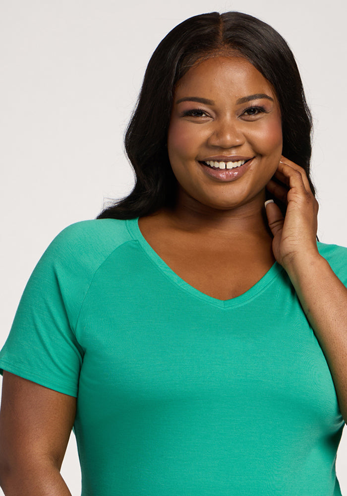 A smiling woman in the Woolx Mia V Neck - Jungle touches her face, posing against a plain background.