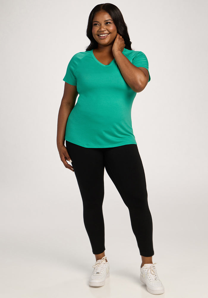 Woman smiling in a Woolx Mia V Neck - Jungle, black leggings, and white sneakers against a plain background.
