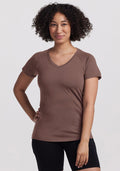 Smiling woman with curly hair wears a Woolx Mia V Neck - Peppercorn and black shorts, one hand on her hip. | Tori is 5'7", wearing a size S
