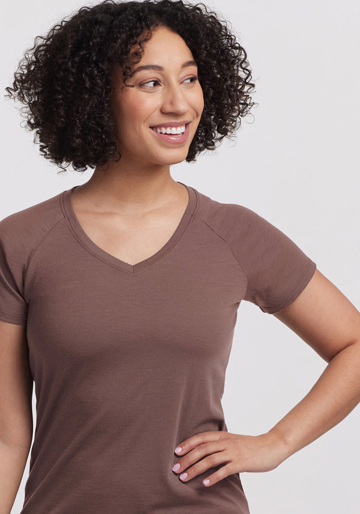 Smiling woman with curly hair wears the Woolx Mia V Neck in Peppercorn, standing confidently against a plain background.