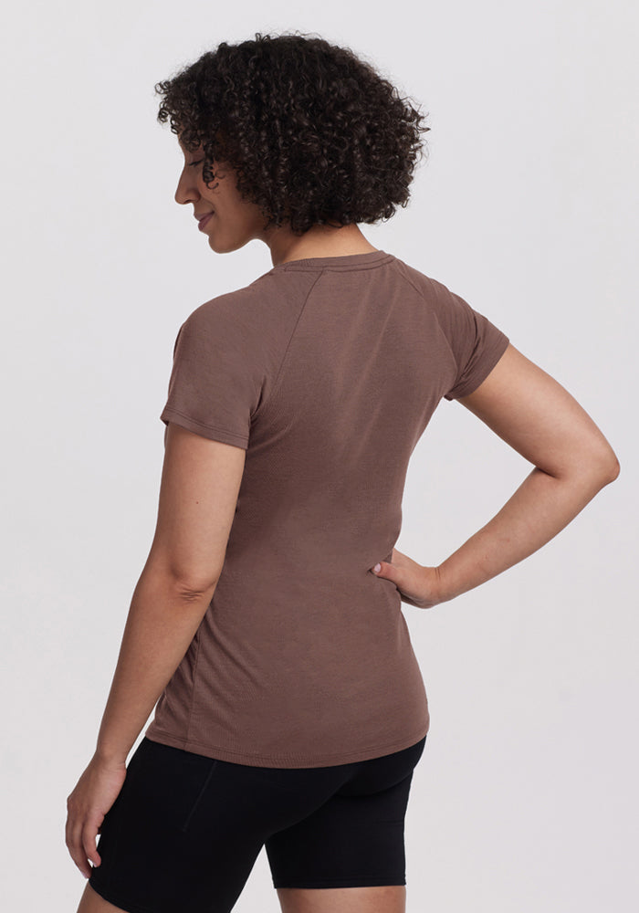 A woman with curly hair wears the Woolx Mia V Neck in Peppercorn and black shorts against a plain background.