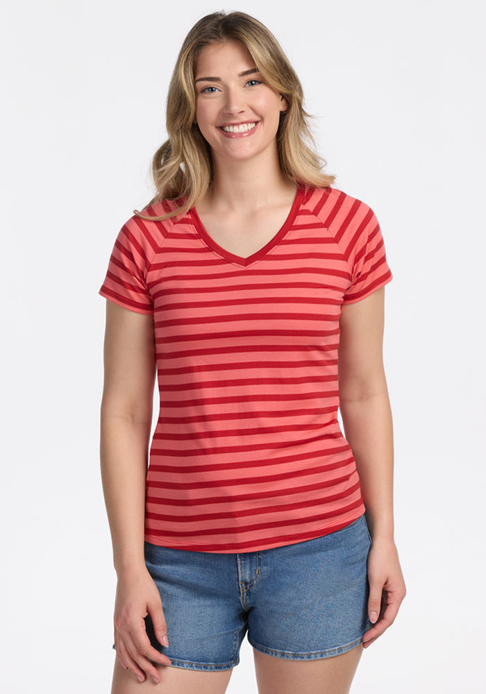A smiling woman with long, light brown hair wears the Woolx Mia V Neck in Wildberry Stripe, paired with blue denim shorts, standing against a plain light background. | Ariana is 5'11", wearing a size S