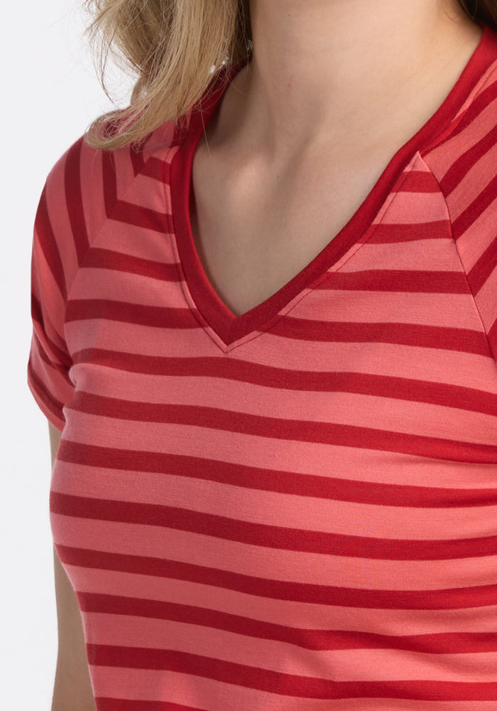A person wearing the Woolx Mia V Neck in Wildberry Stripe, a moisture-wicking T-shirt with red and pink stripes, is shown from shoulders to upper chest against a plain white background.
