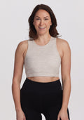 A person with long brown hair, wearing a beige sleeveless top and black leggings, smiles confidently against a white background in a comfortable Woolx Mila Bra - Cream Heather. | Tiffany is 5’8”, wearing a size S
