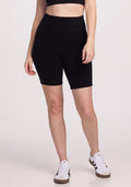 A person is wearing the Woolx Miley Bike Shorts in black along with a matching black crop top. They stand with one hand by their side, also sporting white sneakers with black stripes against a plain white background. | Lilly is 5’9”, wearing a size S