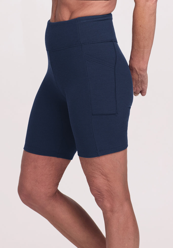 Model wearing Woolx Miley Bike Shorts in Deep Navy, high-waisted with pockets, shown from the side against a plain background.