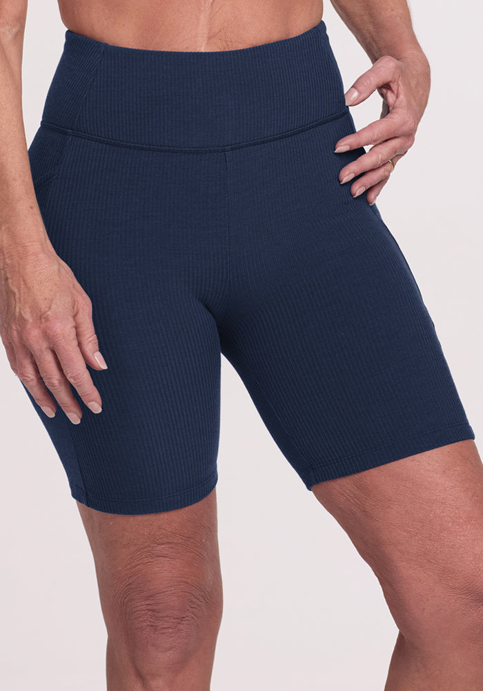 Model wears Woolx Miley Bike Shorts in Deep Navy, standing with one hand on hip against a light background.