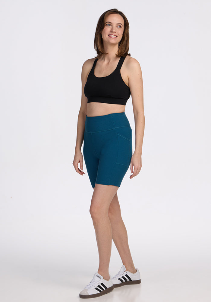 Woman in Woolx Miley Bike Shorts in Moroccan Blue stands smiling against a white background.