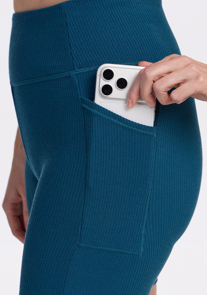 A hand places a smartphone into the side pocket of Woolx Miley Bike Shorts in Moroccan Blue.