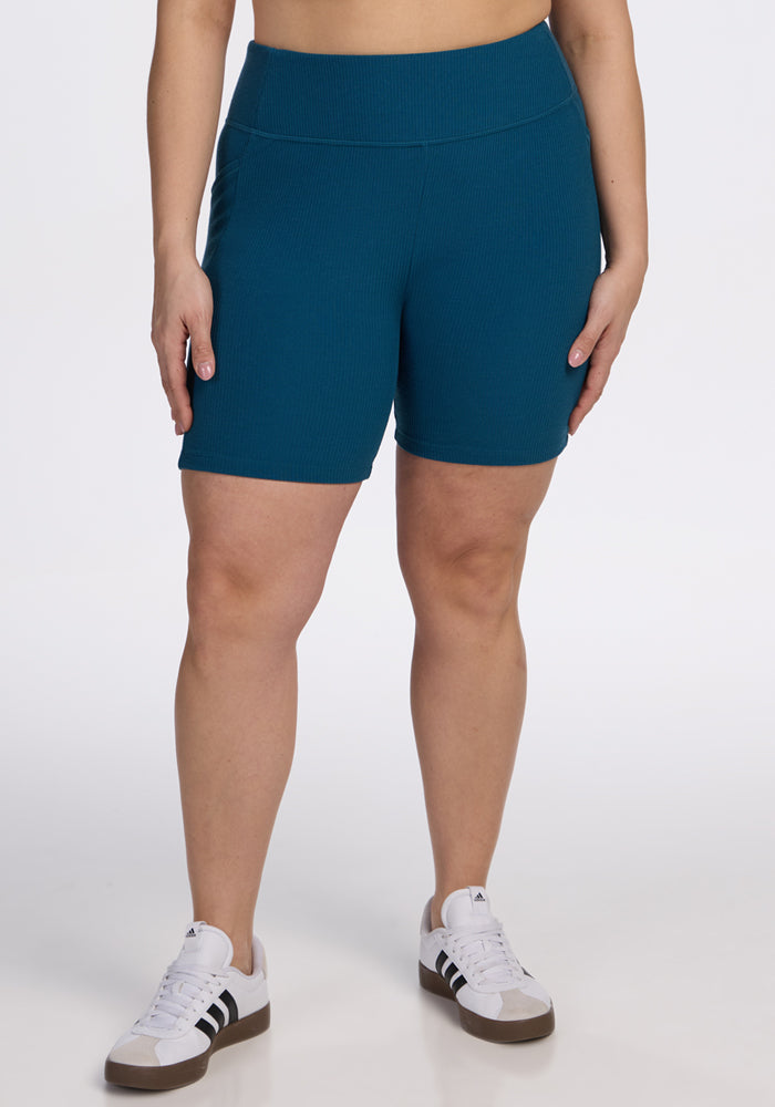 Person wearing Woolx Miley Bike Shorts in Moroccan Blue and white sneakers, standing against a plain white background.