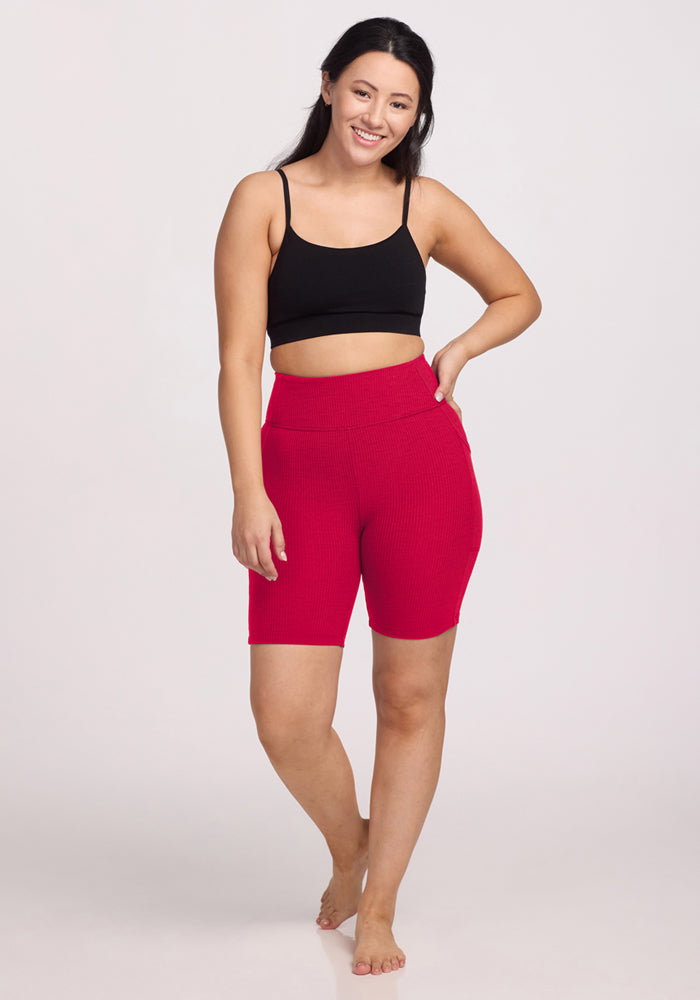 Smiling woman in Woolx Miley Bike Shorts • Final Sale - Poppy Spark, black crop top, hand on hip against plain background.