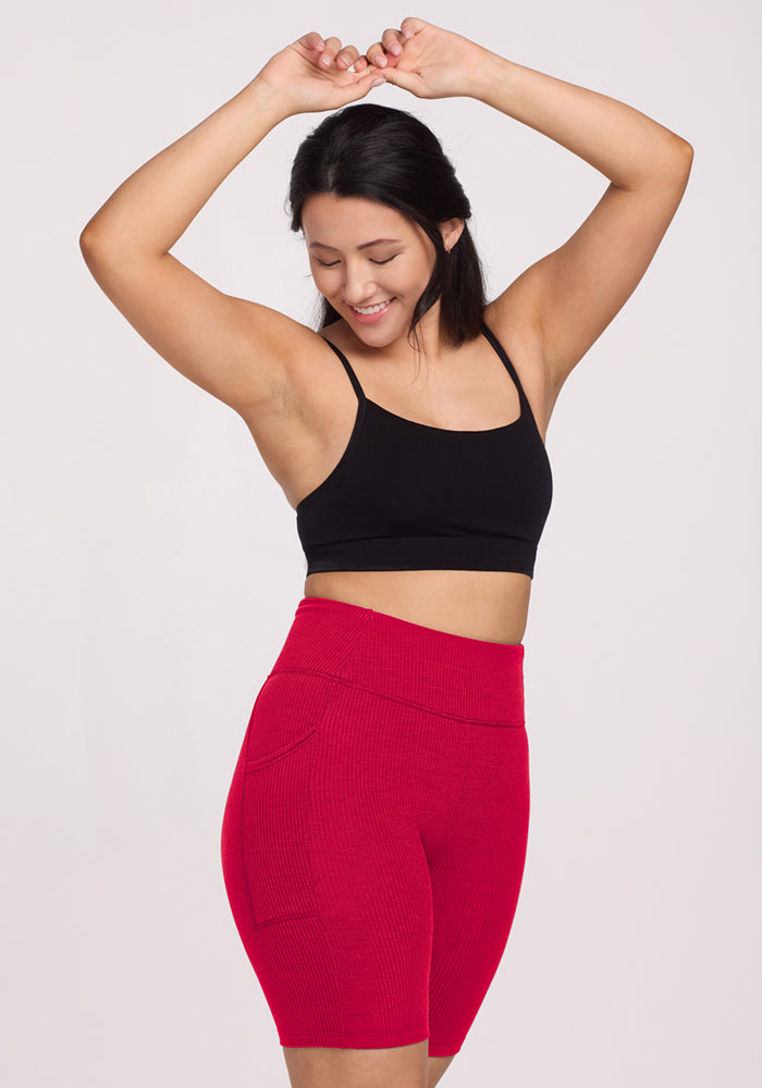 Woman smiling with arms raised, wearing Woolx Miley Bike Shorts • Final Sale - Poppy Spark and a black sports bra.