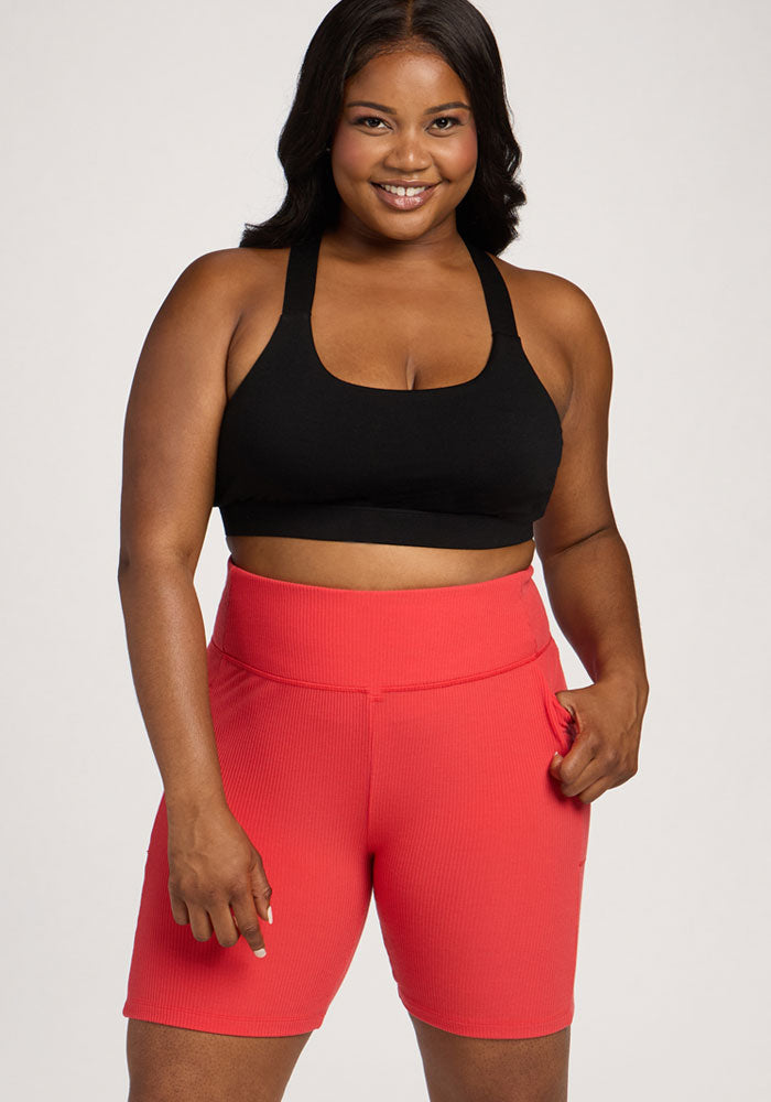 Woman smiles in Woolx Miley Bike Shorts - Hibiscus and a black sports bra, standing against a light background.