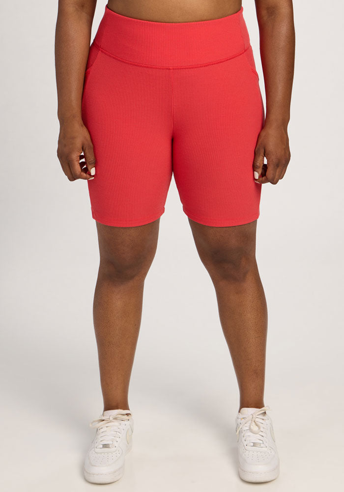 Person wearing Woolx Miley Bike Shorts in Hibiscus and white sneakers, standing against a plain light background. | Sapphire is 5’8”, wearing a size XL
