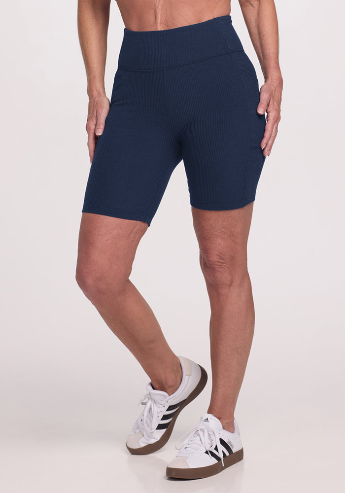 Someone in Woolx Miley Bike Shorts in Deep Navy and white sneakers stands against a plain light background.