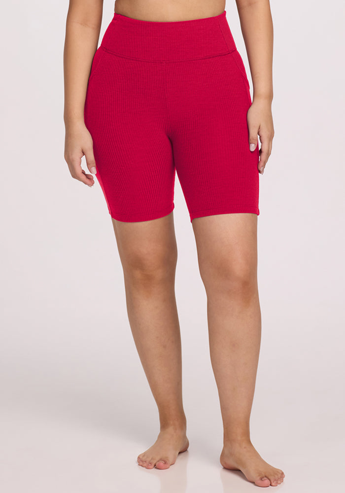 A person stands barefoot wearing Woolx Miley Bike Shorts in Poppy Spark, with a plain light background.