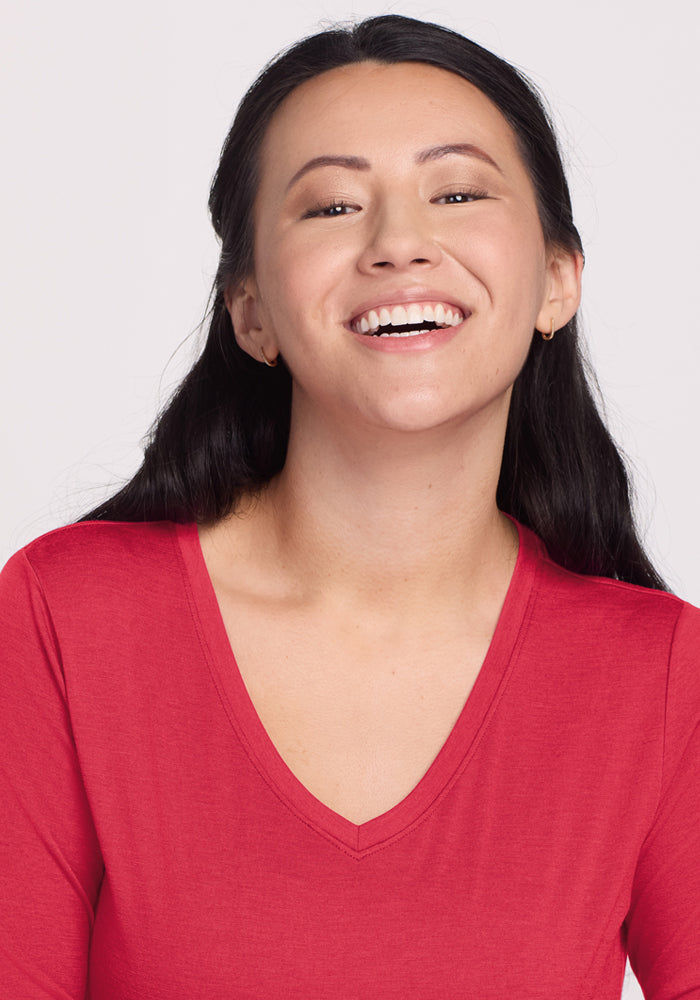 Woman with long dark hair smiles in a Woolx Millie Long Sleeve - Berry Ice Pop top, against a plain light background.