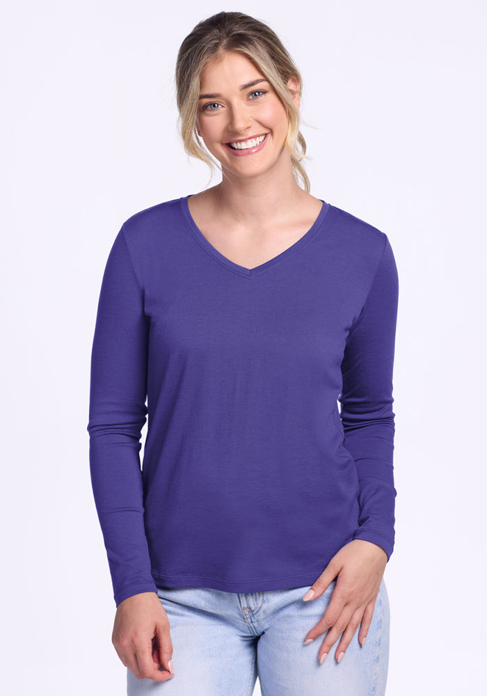 A smiling woman wears the Woolx Millie Long Sleeve in Berry Indigo and light blue jeans against a plain background. | Ariana is 5'11", wearing a size S