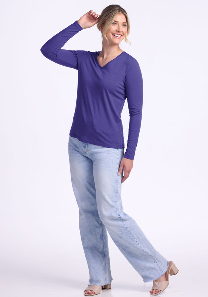 Woman in a Woolx Millie Long Sleeve - Berry Indigo and light blue jeans smiles with one hand raised, on a white background.