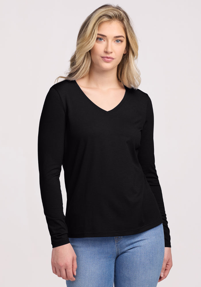 A person with long hair is wearing the Woolx Millie Long Sleeve in black and blue jeans, standing against a plain background. They face the camera with a neutral expression. | Ariana is 5'11", wearing a size S