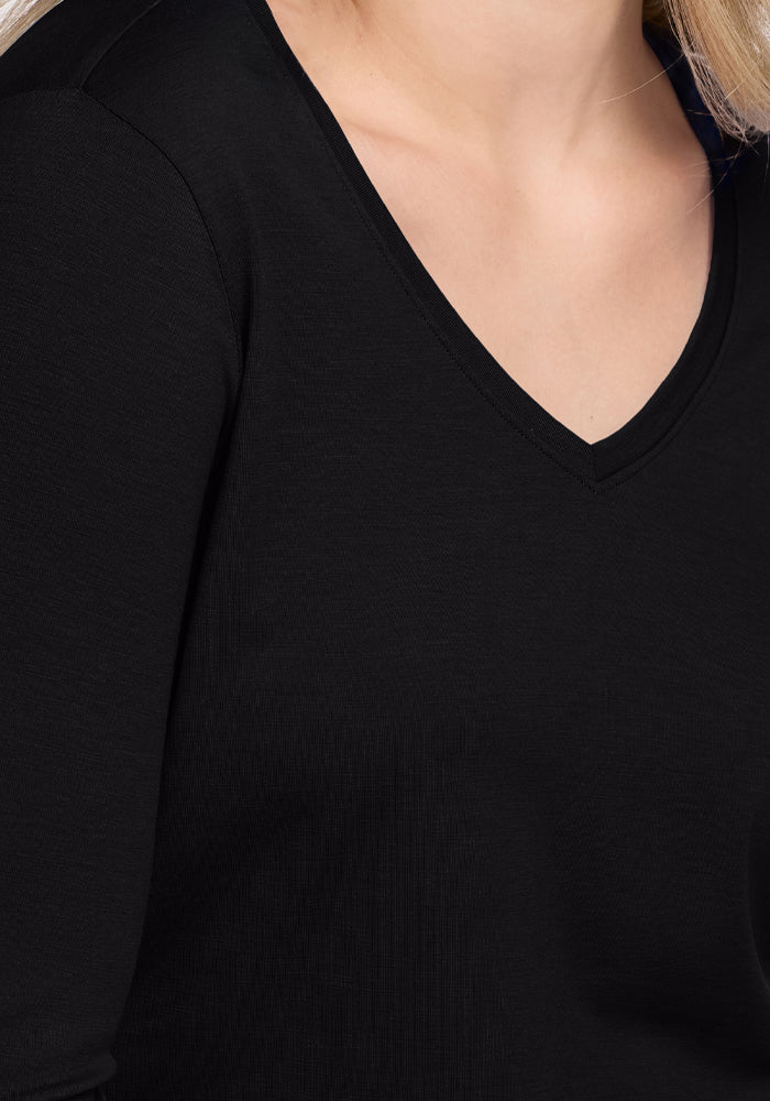 A person wears the Woolx Millie Long Sleeve in black, crafted from merino wool. The design accentuates the torso and shoulders, showcasing the fabric's elegance and temperature-regulating qualities. Light hair softens the frame's composition.