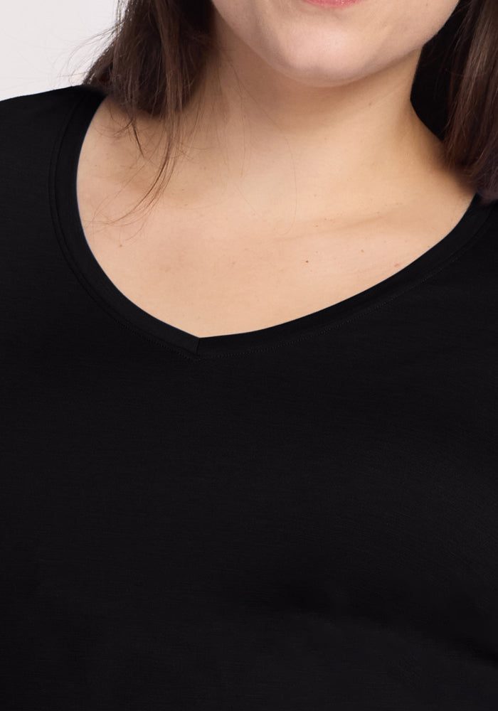 A person with long brown hair is pictured from the shoulders up, wearing the Woolx Millie Long Sleeve - Black. The moisture-wicking V-neck shirt is stylishly presented with part of the person's face visible.