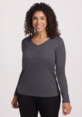 Smiling woman in Woolx Millie Long Sleeve, Cinder Melange, with curly hair and black pants against a light background.