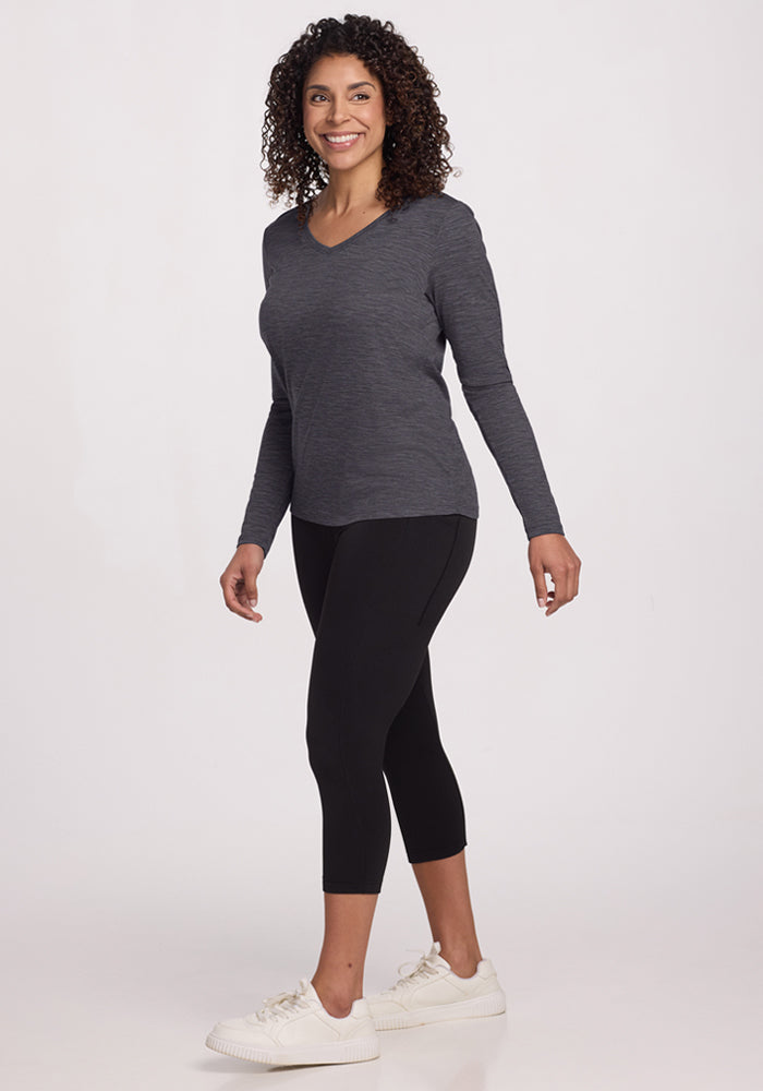 Woman with curly hair wearing the Woolx Millie Long Sleeve in Cinder Melange, black leggings, and white sneakers, smiling.