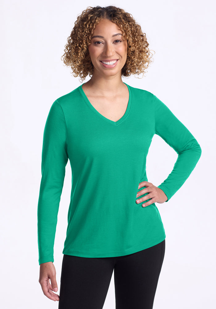 Smiling woman with curly hair wears Woolx Millie Long Sleeve - Jungle and black pants, one hand on her hip. | Tori is 5'7", wearing a size S