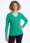 Smiling woman with curly hair wears Woolx Millie Long Sleeve - Jungle and black pants, one hand on her hip. | Tori is 5'7", wearing a size S