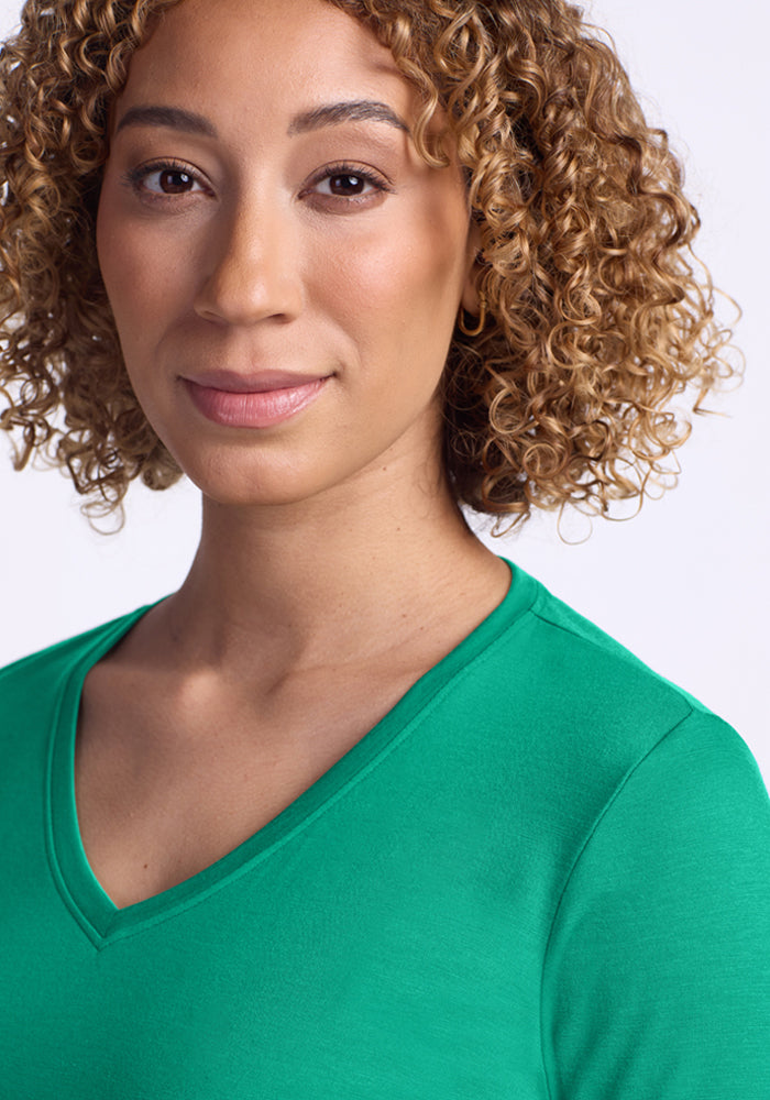 A woman with curly hair wears the Woolx Millie Long Sleeve in Jungle and smiles softly, facing the camera.