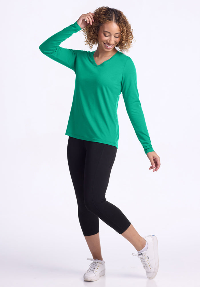 Woman in Woolx Millie Long Sleeve - Jungle, black leggings, and white sneakers smiling against a white background.